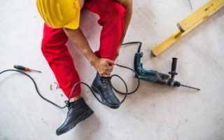 An accident of an unrecognizable male worker at the construction site. A man with an injured leg sitting on the floor. Top view.